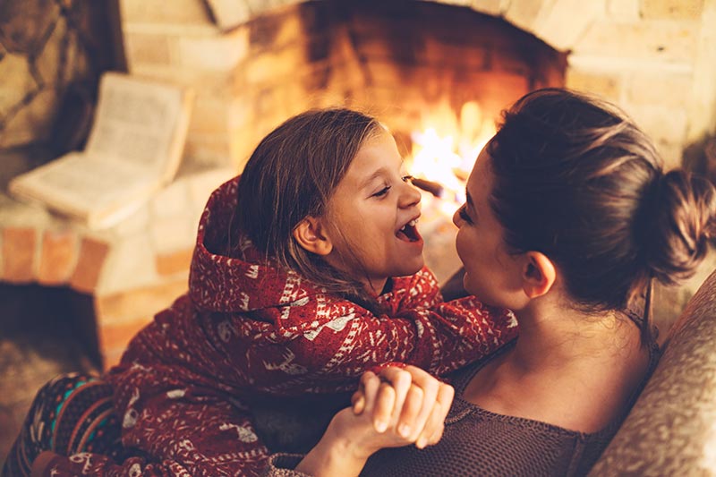 Mother and daughter cuddling by a fireplace
