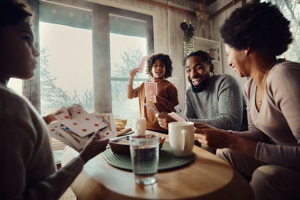 a family sits around a table in the living room laughing and playing cards