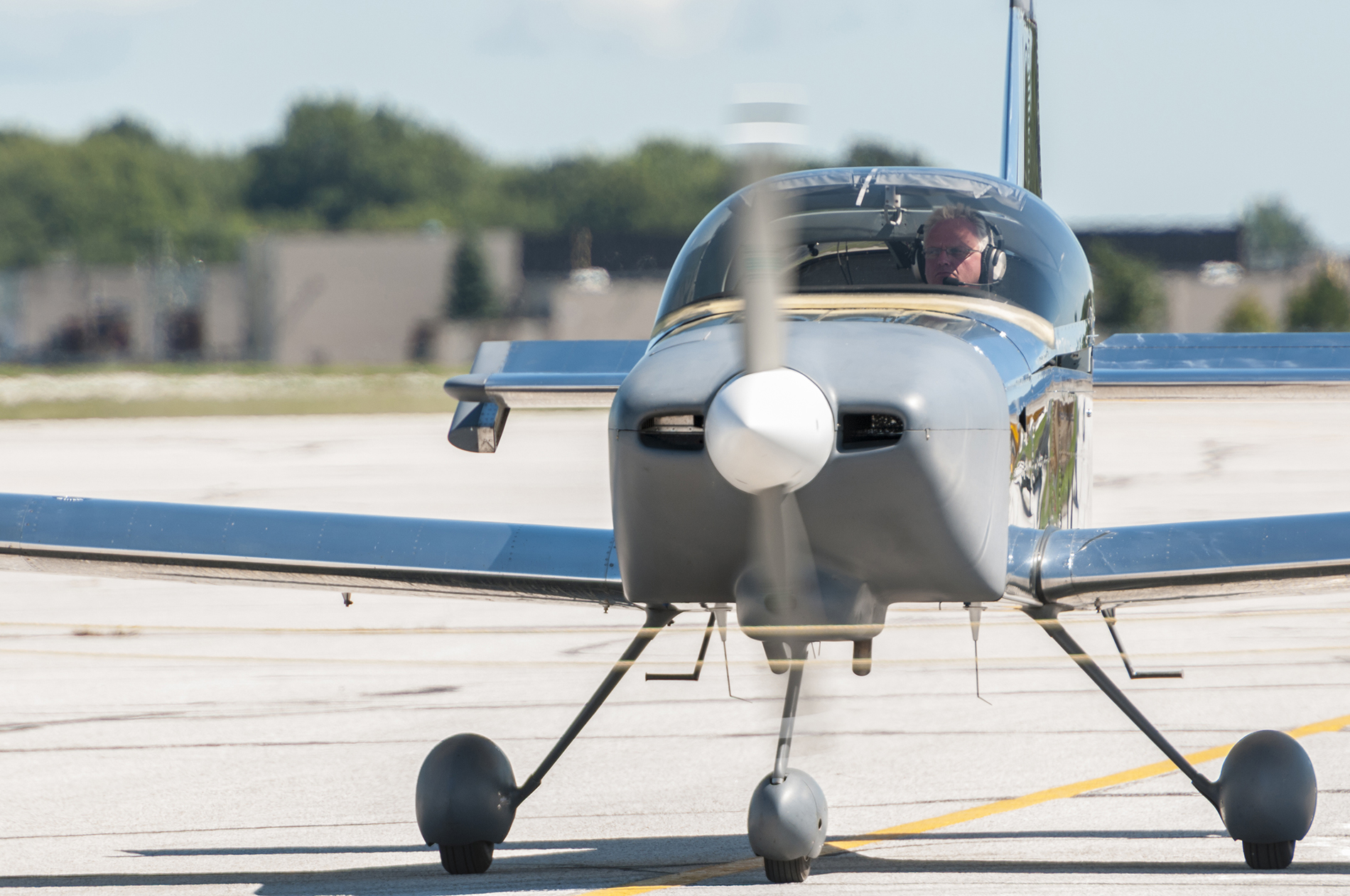 Pilot inside the cockpit of a small blue and yellow plane on a runway